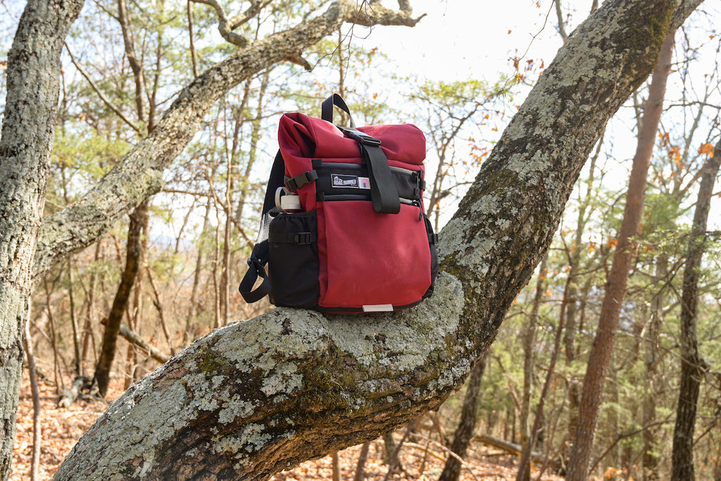 Medium Roll Top in the Woods seen in Burgundy Cordura sitting on a tree branch.