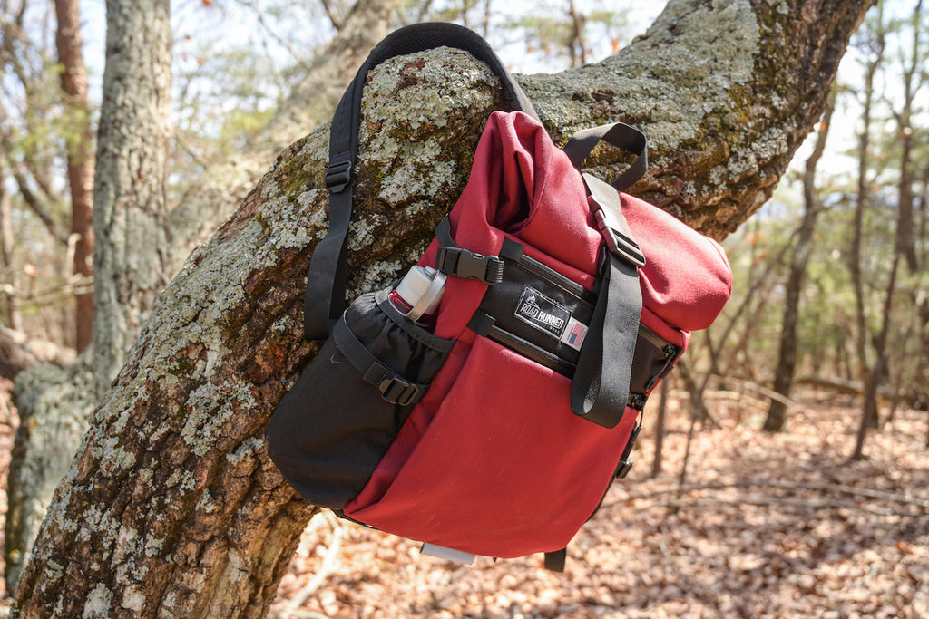 Medium Roll Top in the Woods seen in Burgundy Cordura hanging on a tree branch.